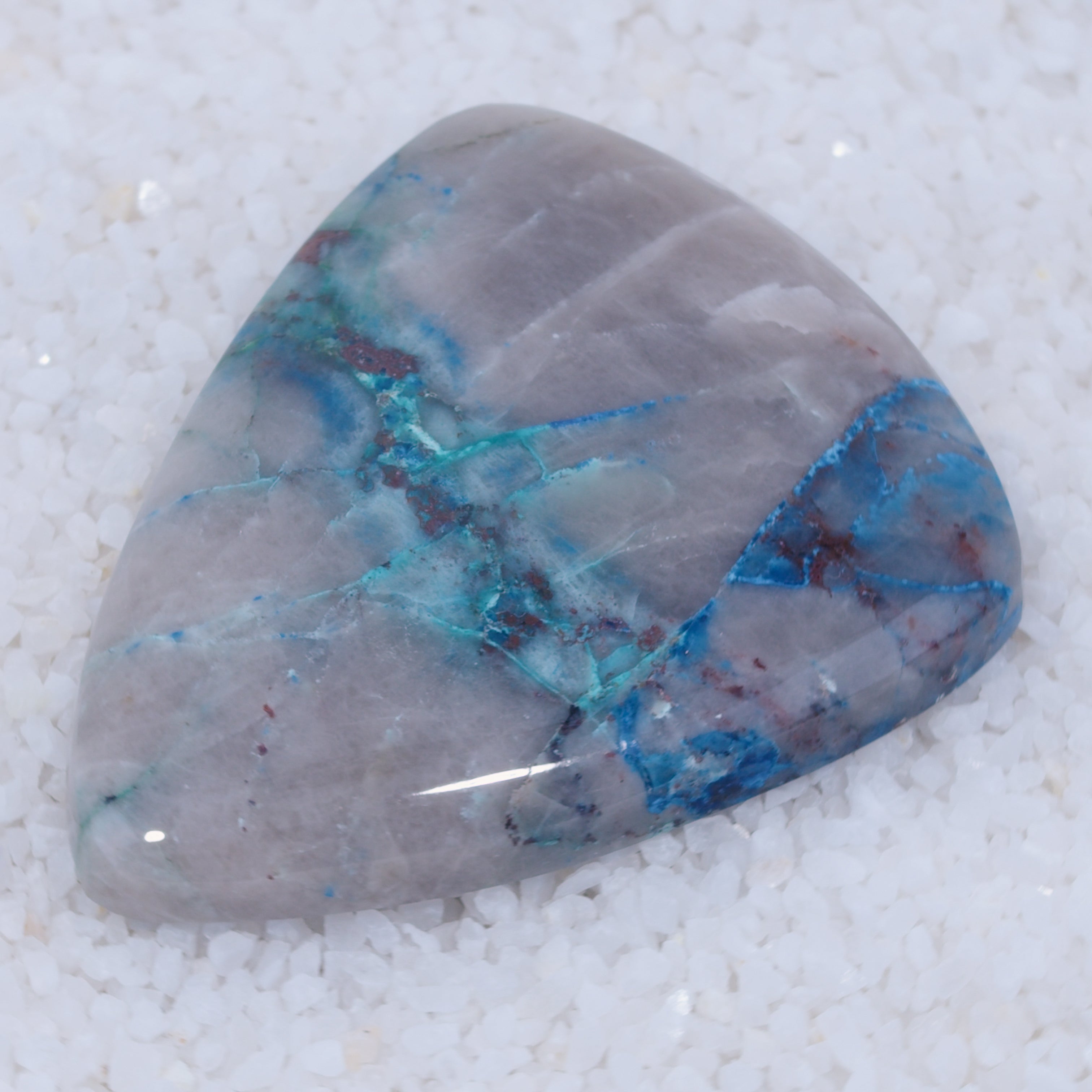 Triangular Canyonite stone with blue and red patterns on a white background