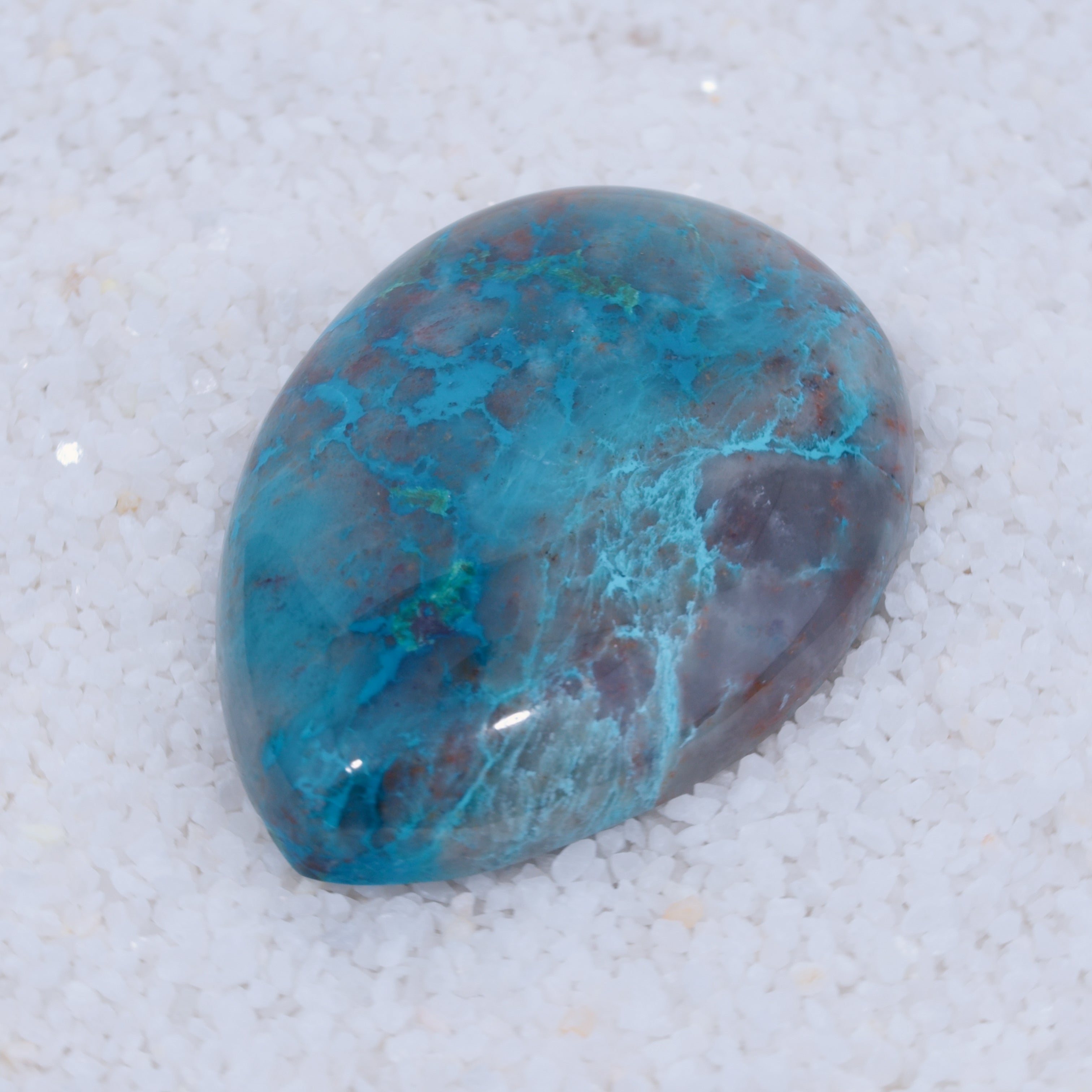 Turquoise colored Canyonite stone on a white sandy background