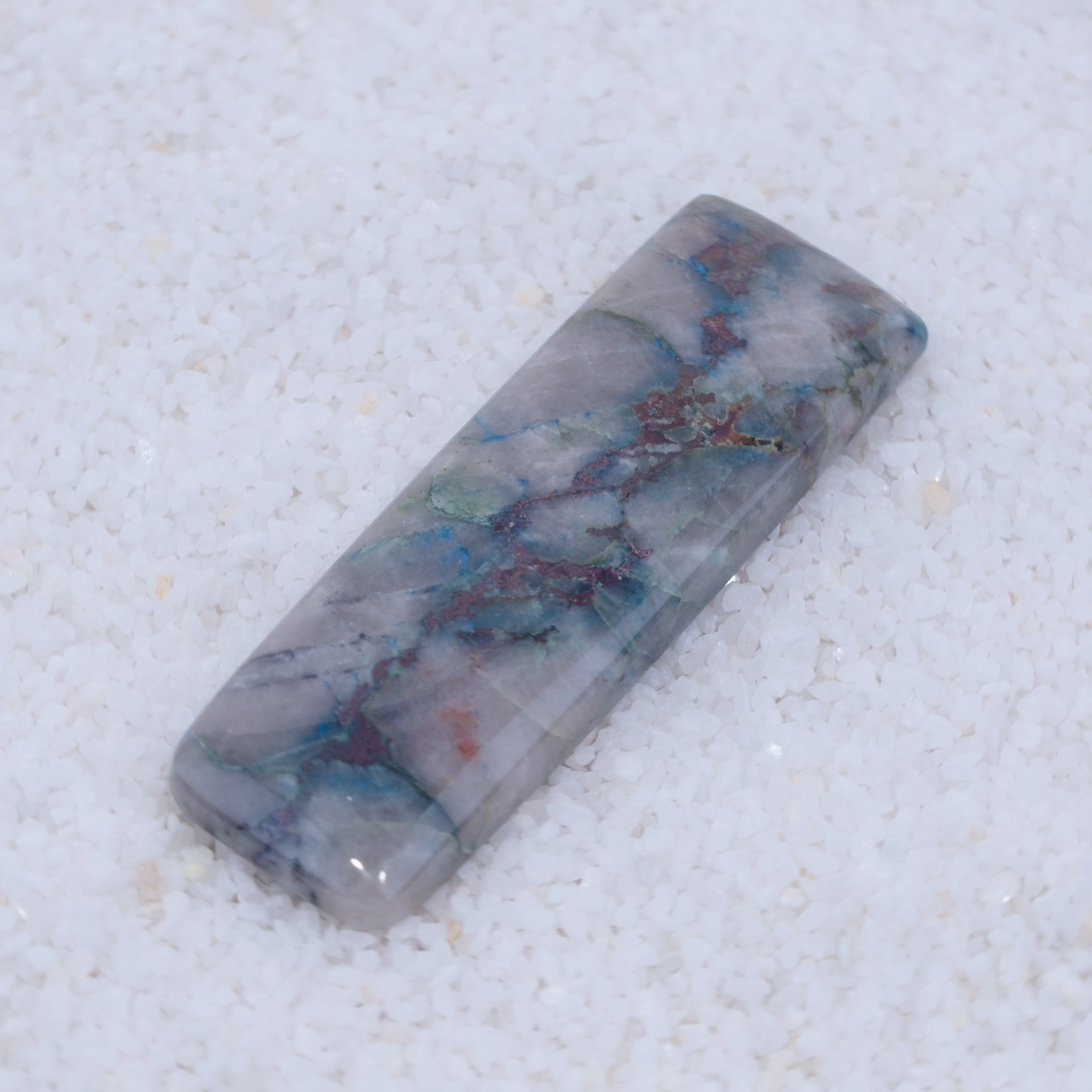 Polished Canyonite stone with blue and red patterns on a white background