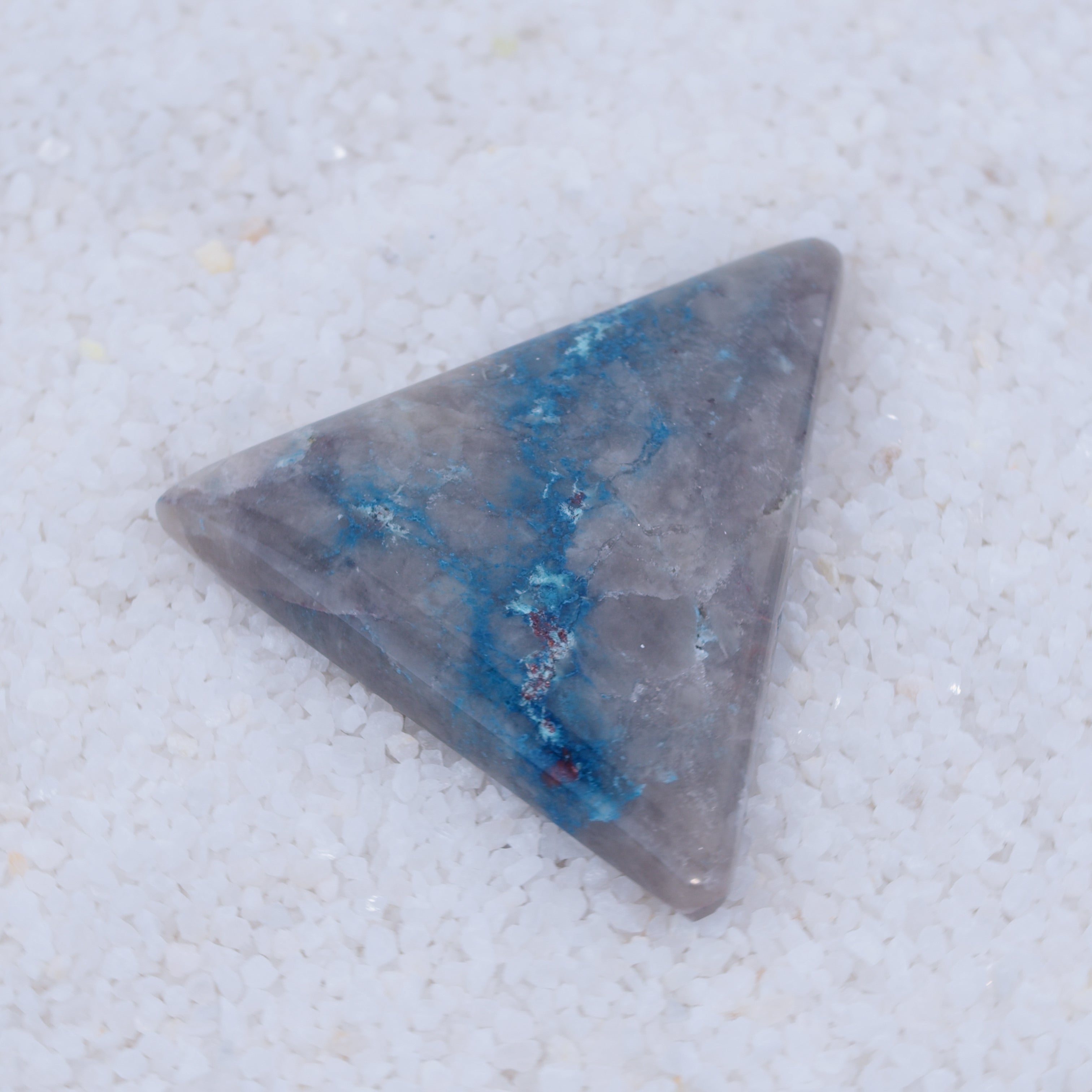 Triangular Canyonite crystal with blue inclusions on a light gray background