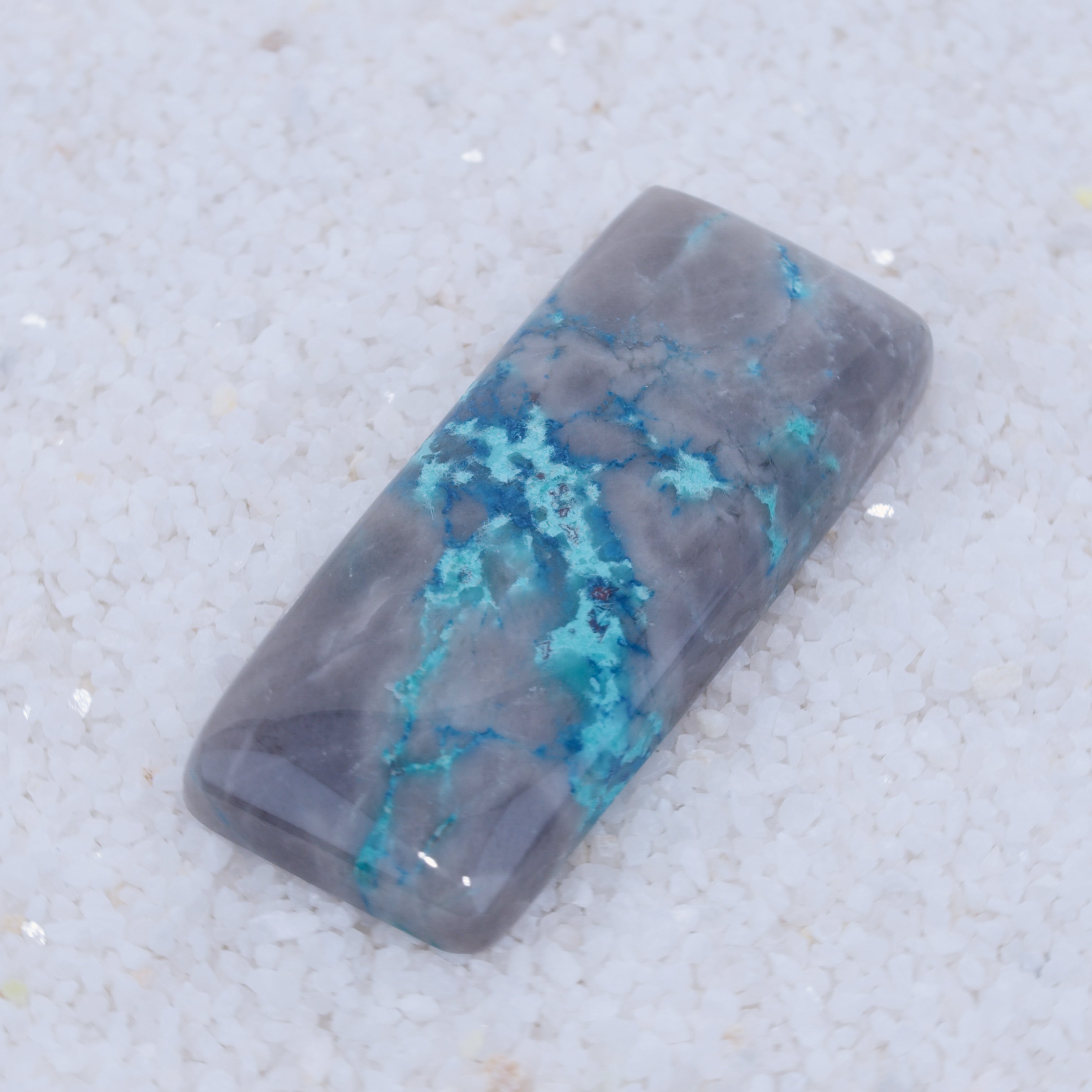 Rectangular Canyonite stone with blue veins on a textured white background