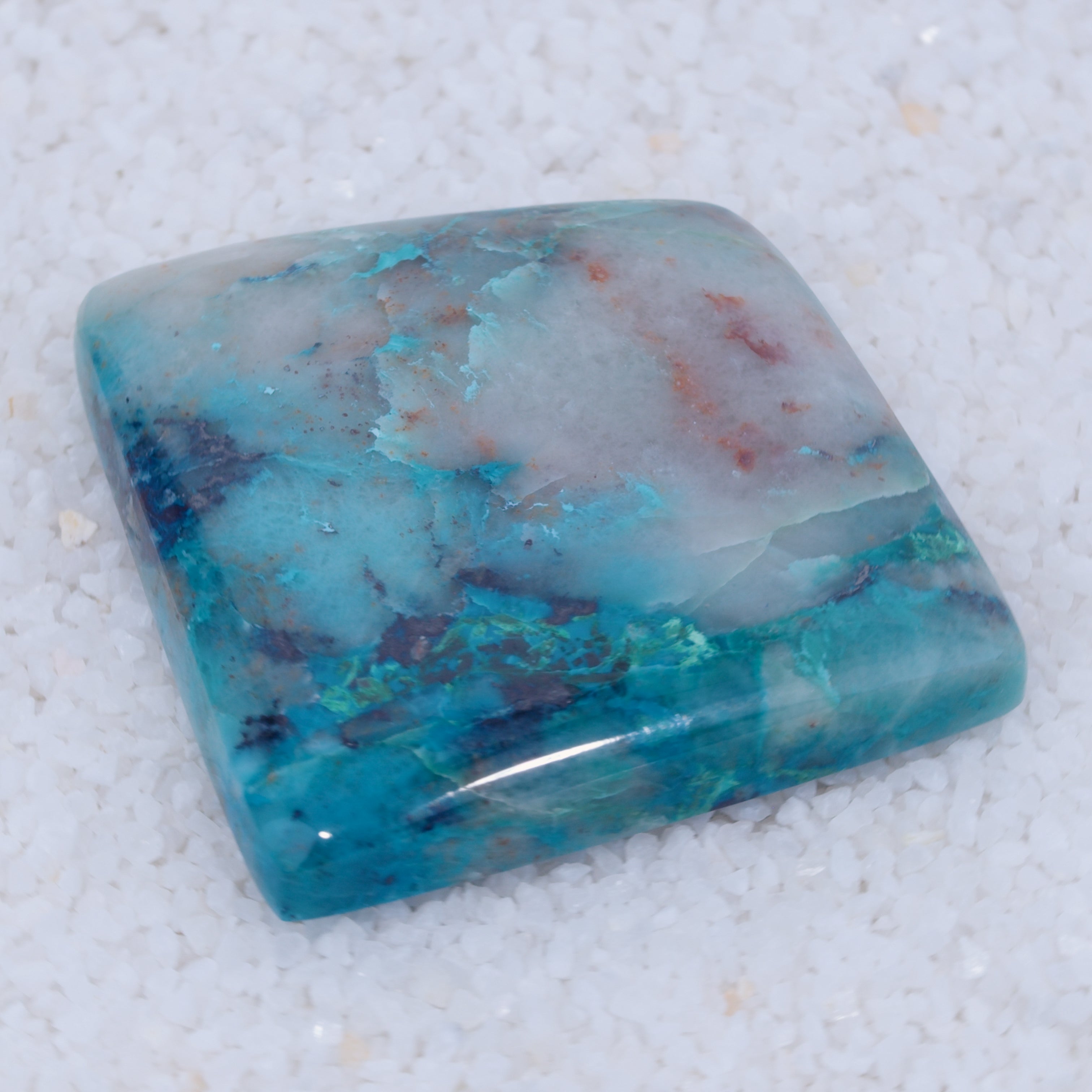 Polished turquoise colored Canyonite stone on a textured white background
