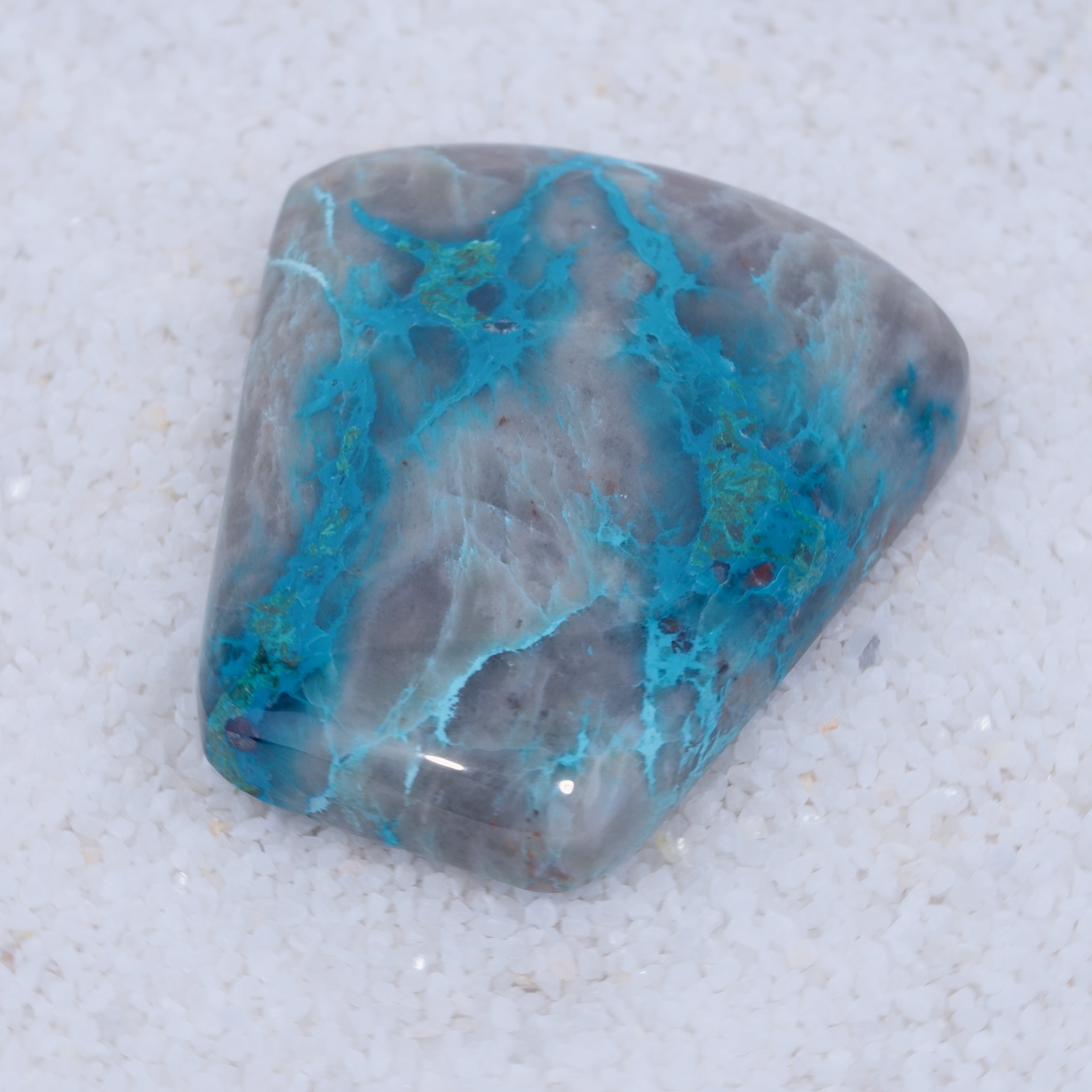 A rare cabochon from Canyonite Sky LTD, this trapezoidal gemstone features fine white crystals and a gray surface marbled with vibrant blue and teal veins, making it a striking piece for collectors.