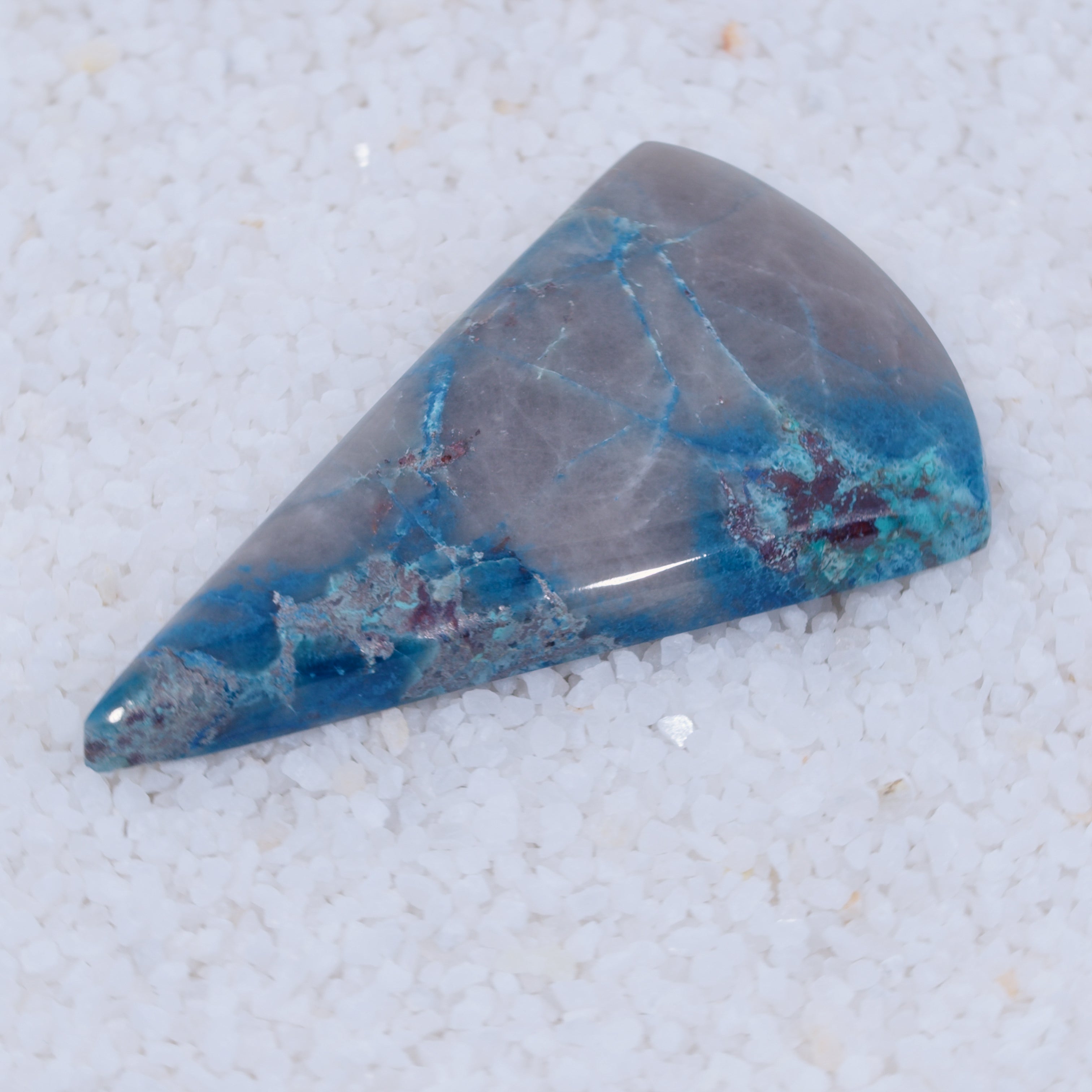 Triangular Canyonite stone with blue and gray patterns on a textured white background