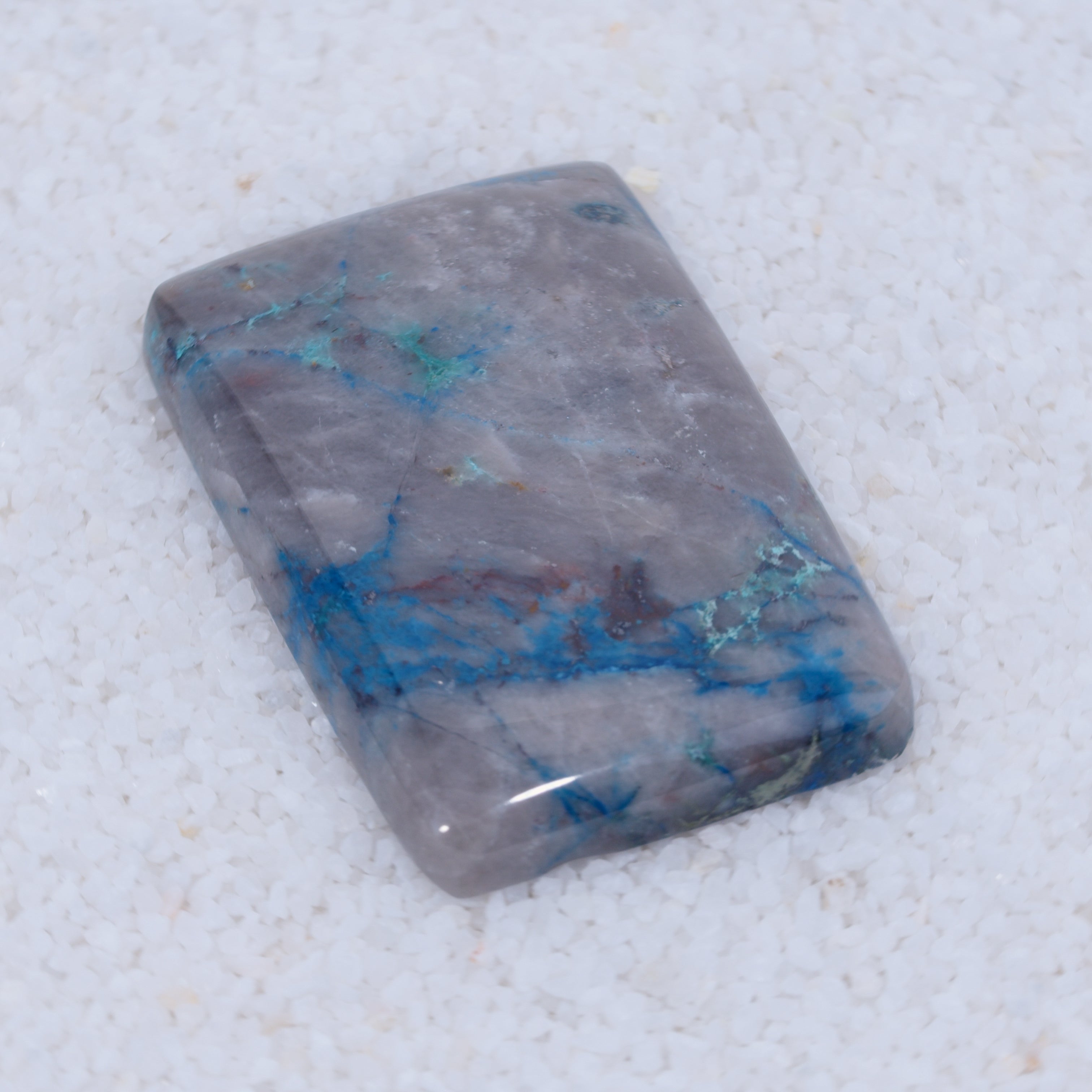 Rectangular Canyonite stone with blue veins on a textured white background