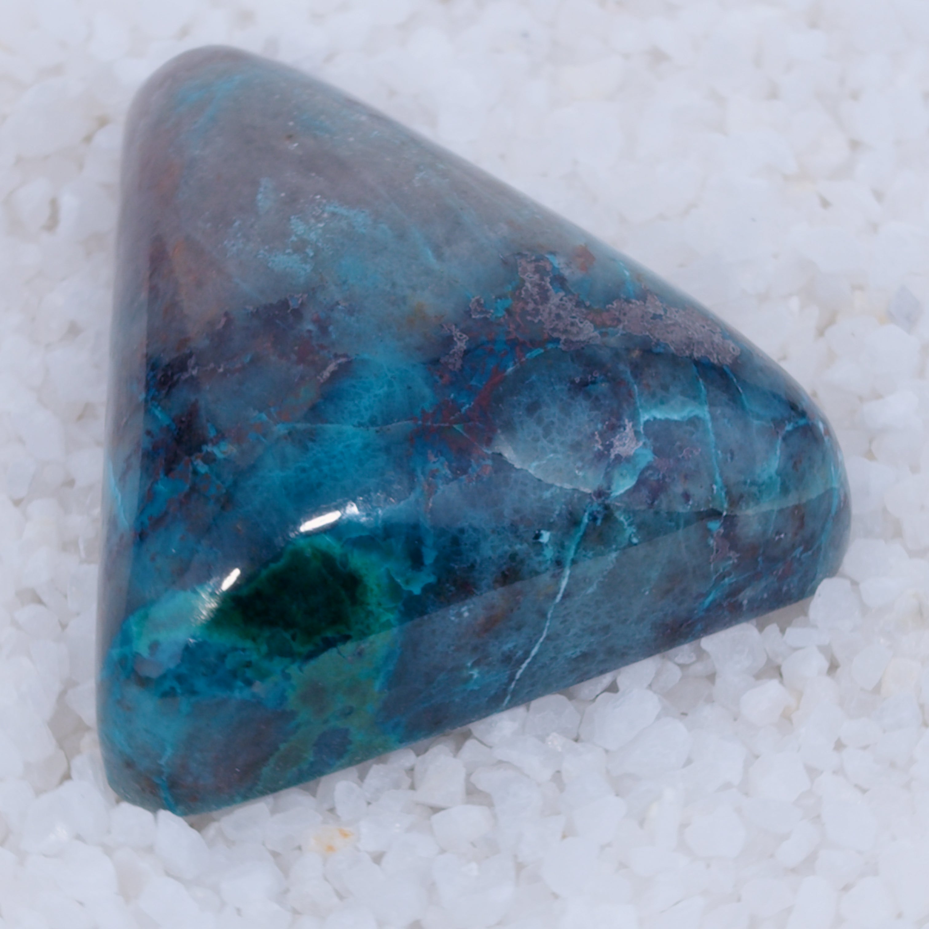 Triangular stone with blue and purple hues on a white sandy background