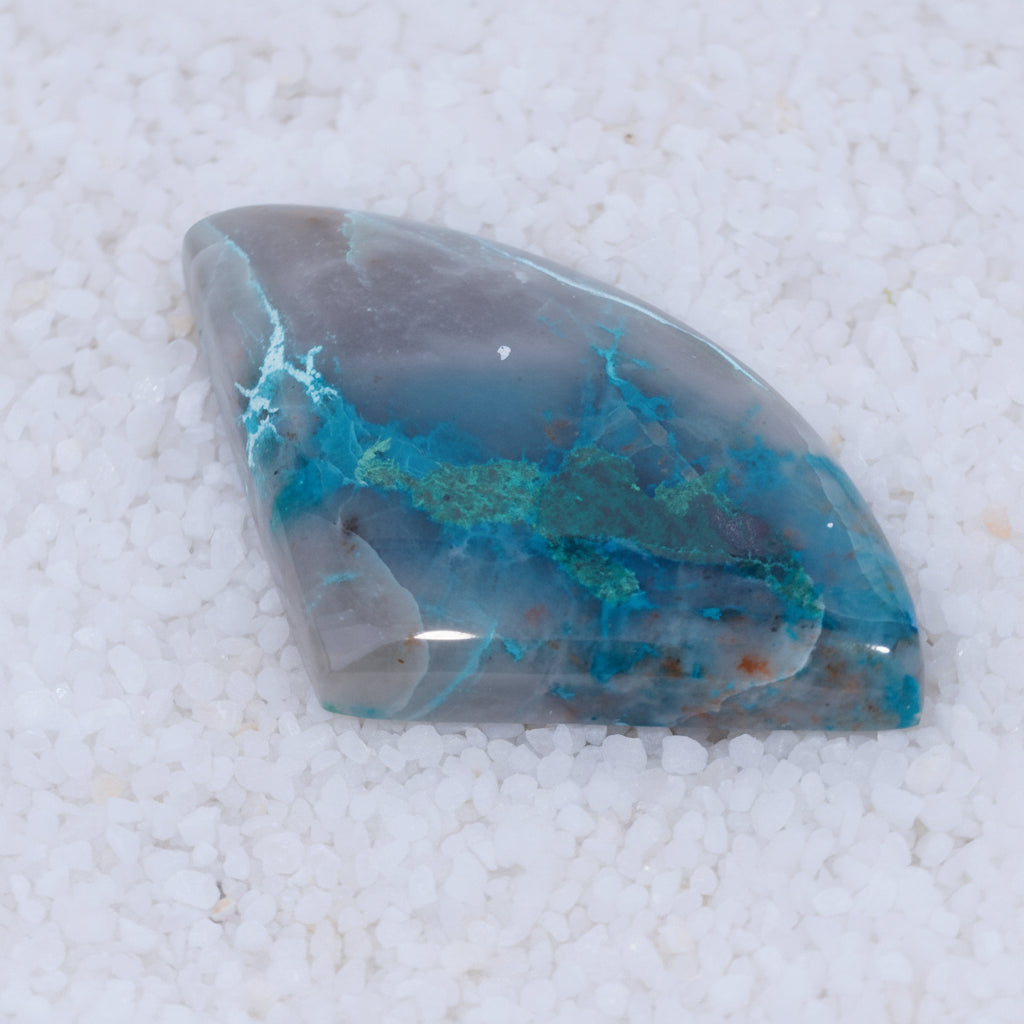 Polished gemstone with blue and gray patterns on a white sand background