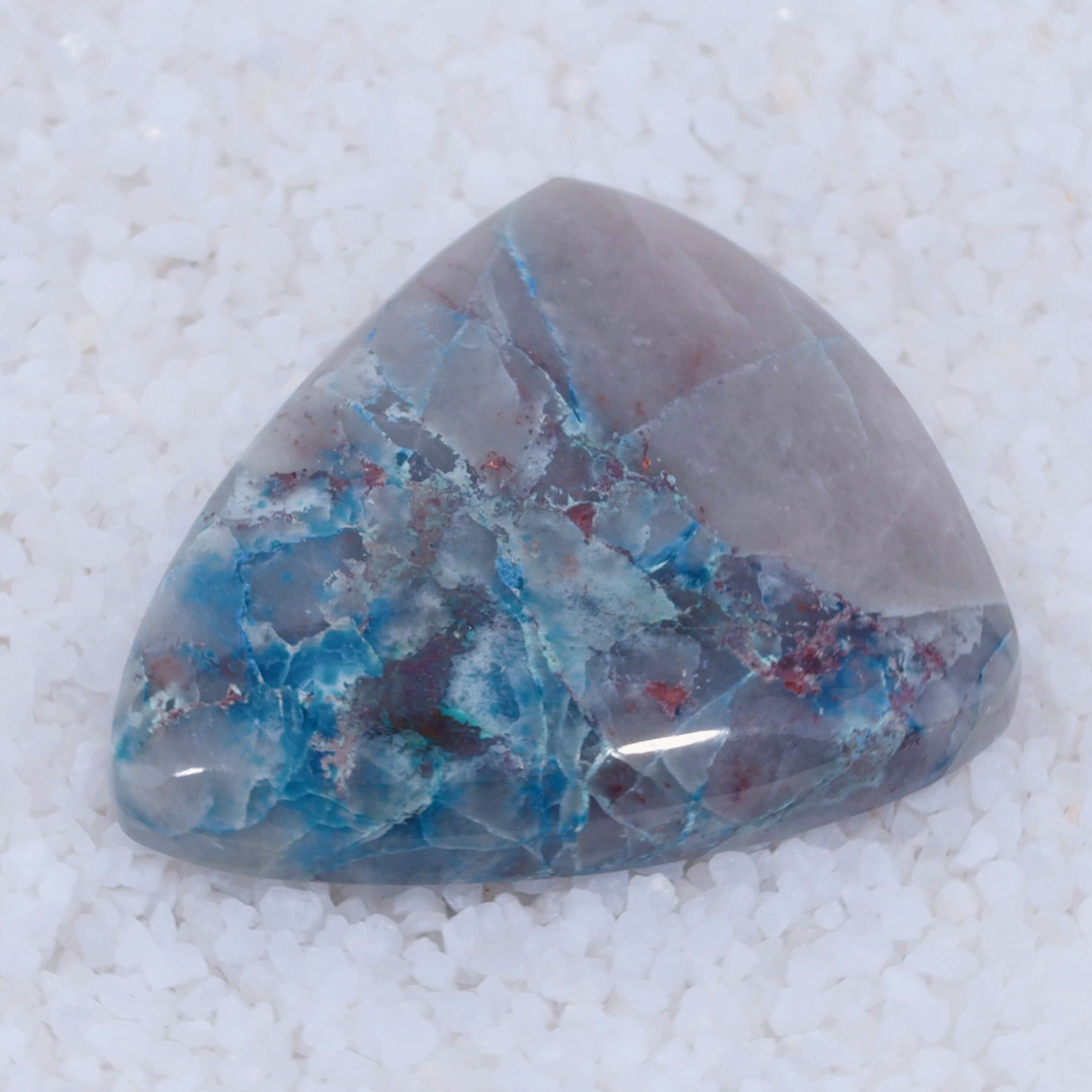 Triangular Canyonite crystal stone with blue and red inclusions on a white background