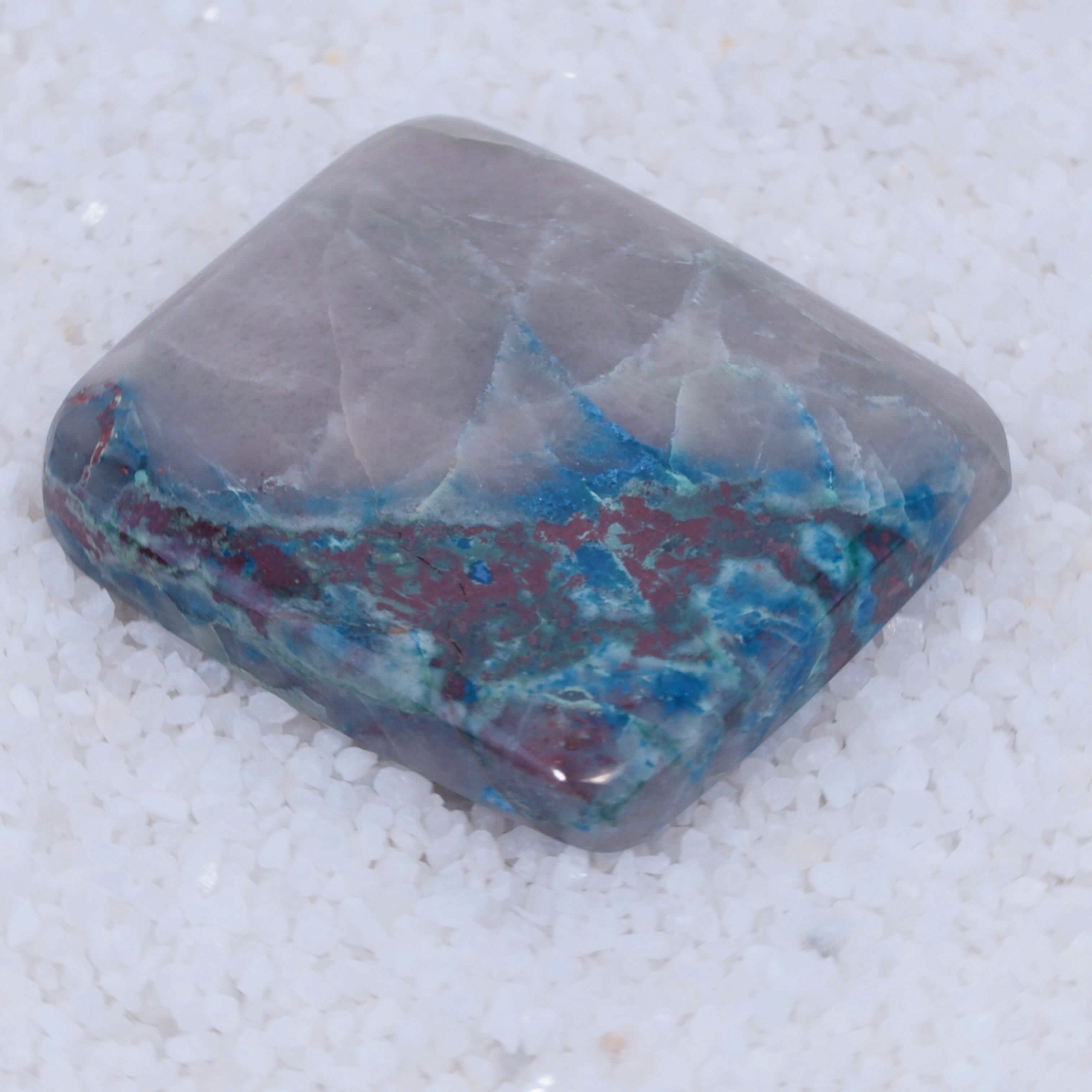 Polished Canyonite gemstone with blue and red inclusions on a white background