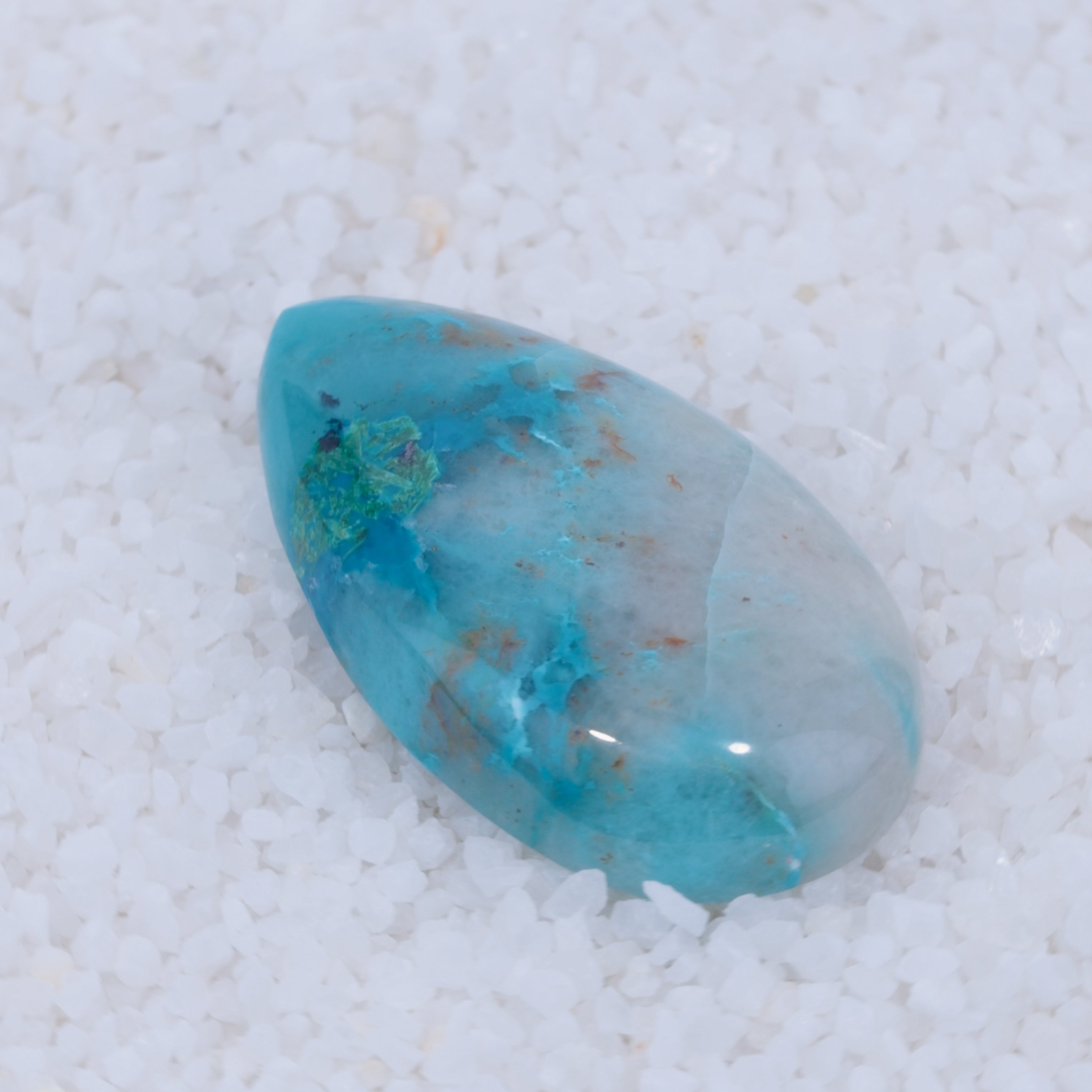 Teardrop-shaped turquoise stone on a textured white background