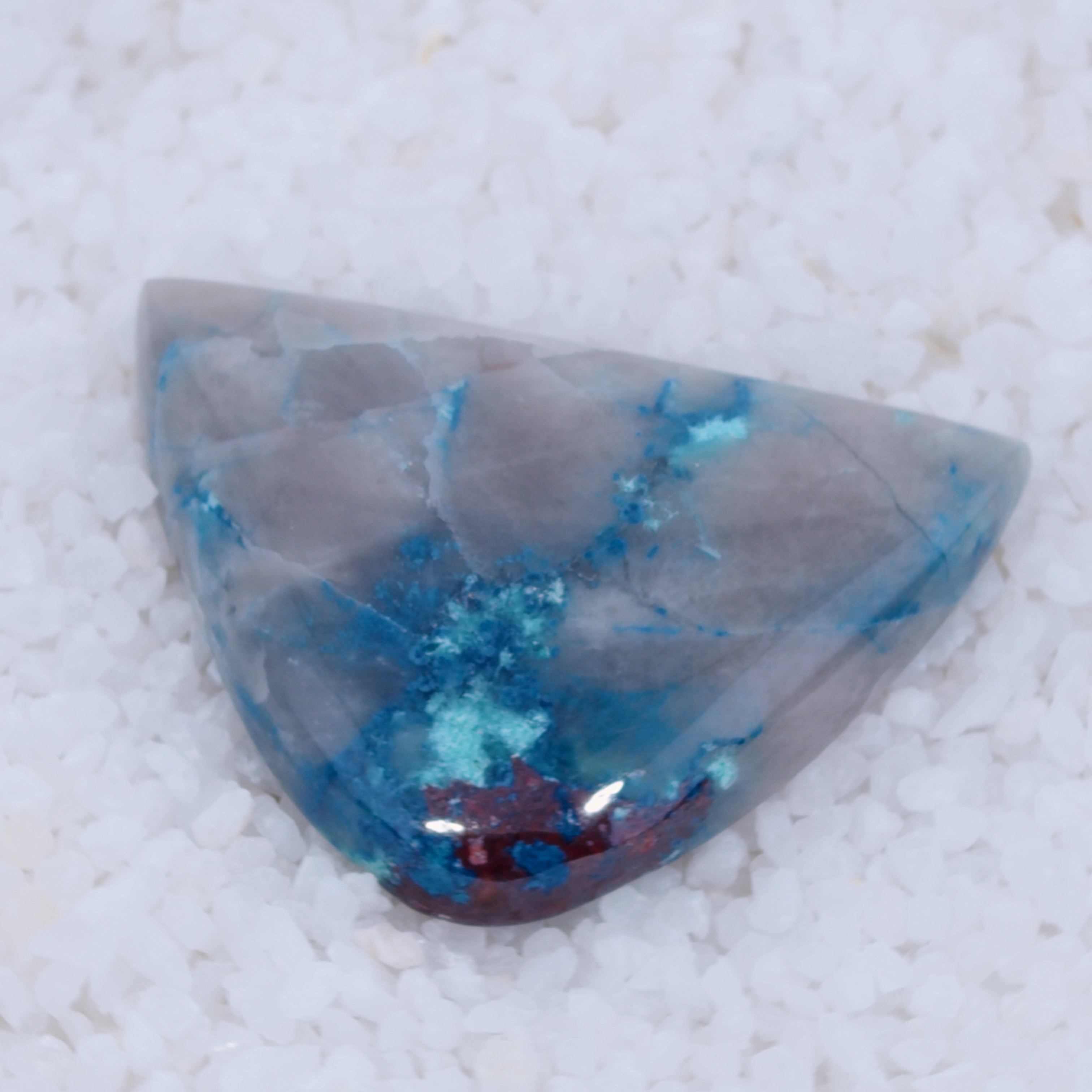 Triangular stone with blue and red inclusions on a textured white background