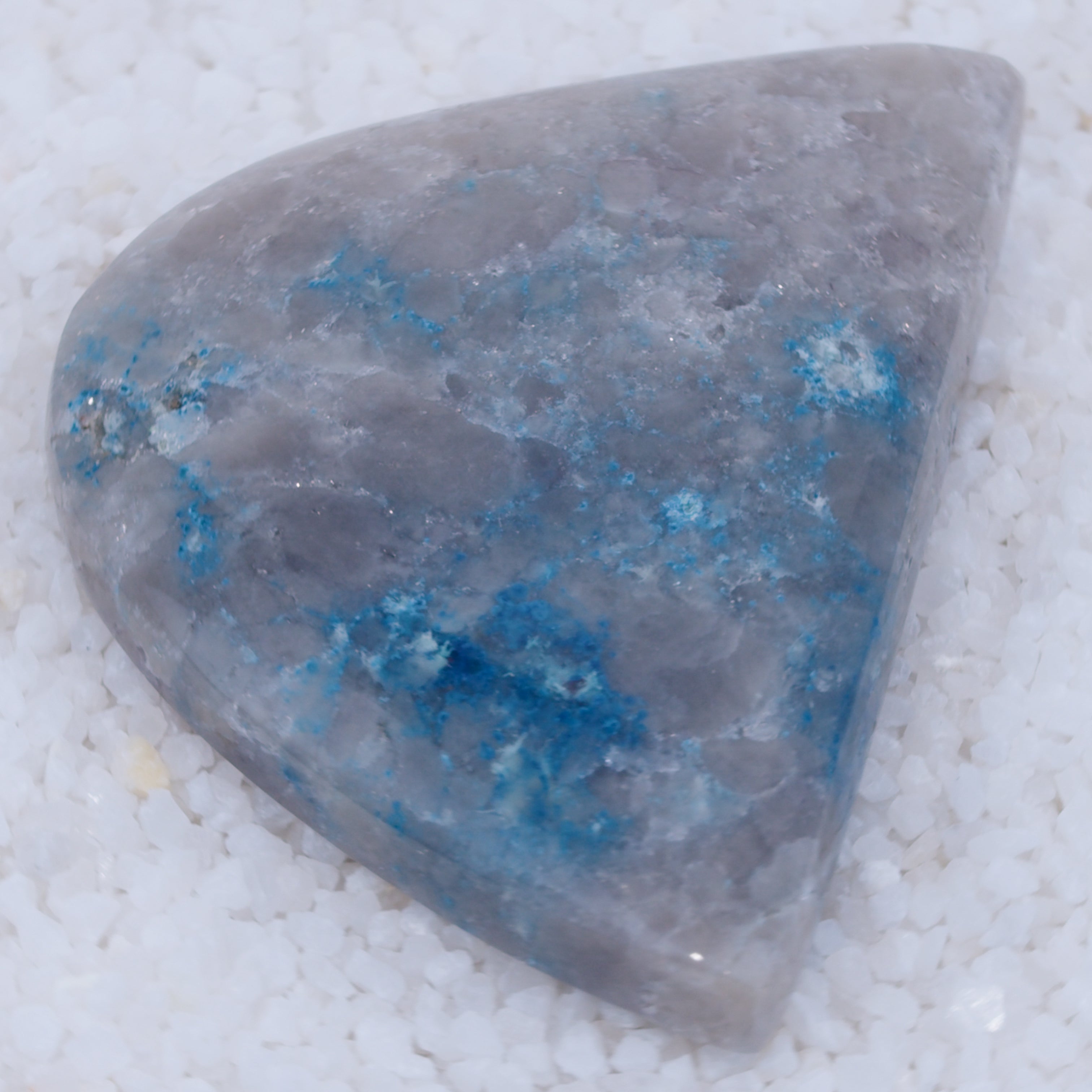 Triangular stone with blue veins on a white sandy background