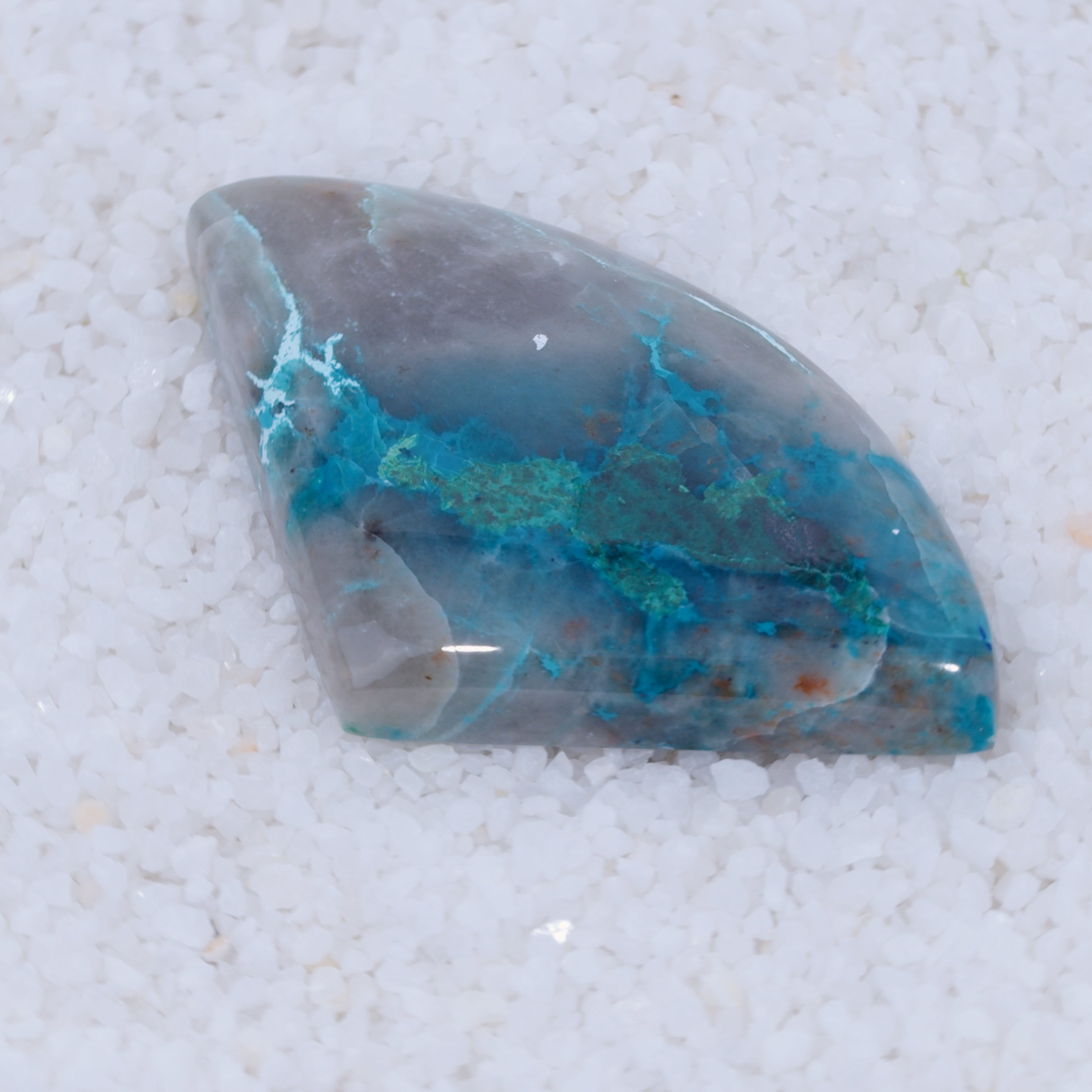Polished gemstone with blue and gray patterns on a white sand background