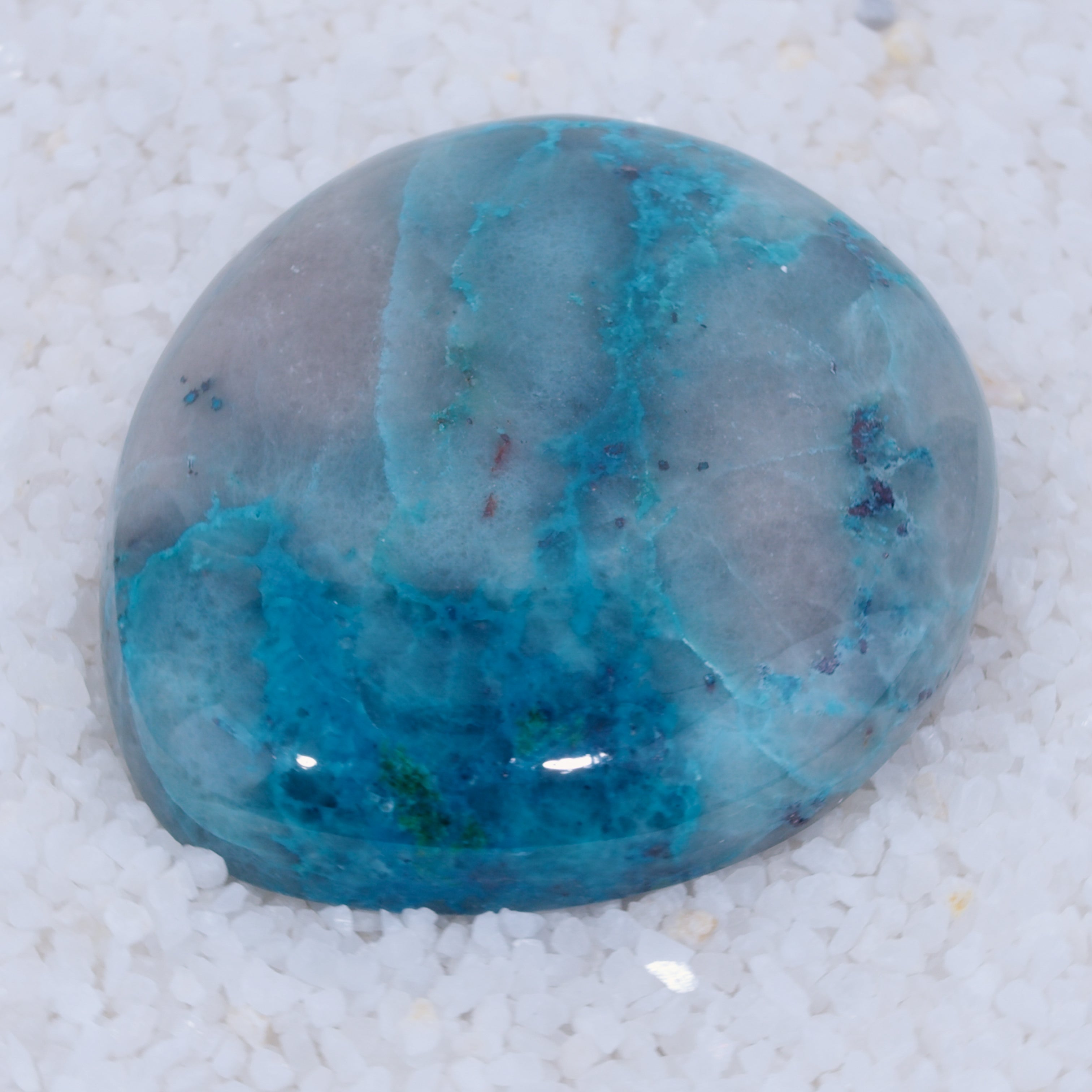 Polished Canyonite gemstone with blue and gray patterns on a white sand background