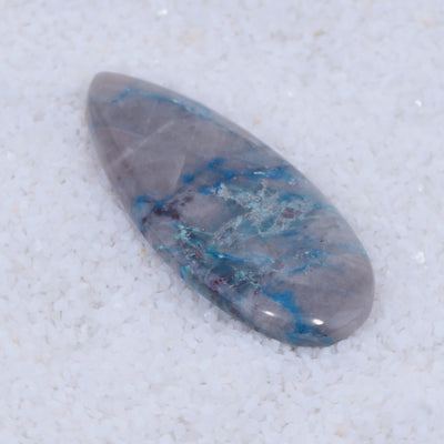 Teardrop-shaped Canyonite stone with blue and gray patterns on a textured white background