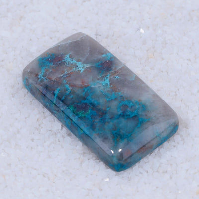 Rectangular Canyonite stone with blue and gray patterns on a textured white background