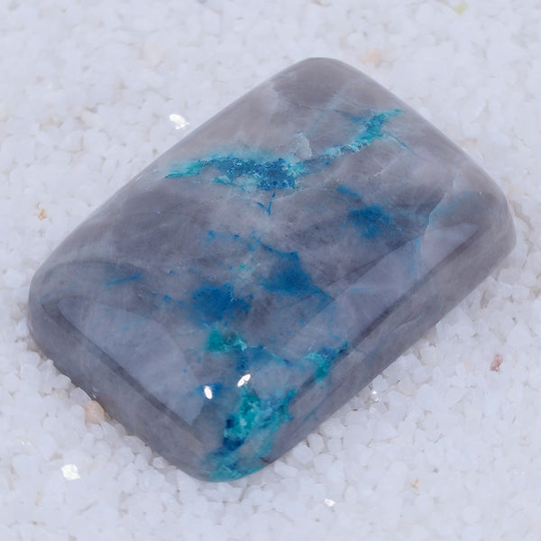 Rectangular Canyonite stone with blue and green inclusions on a textured white background