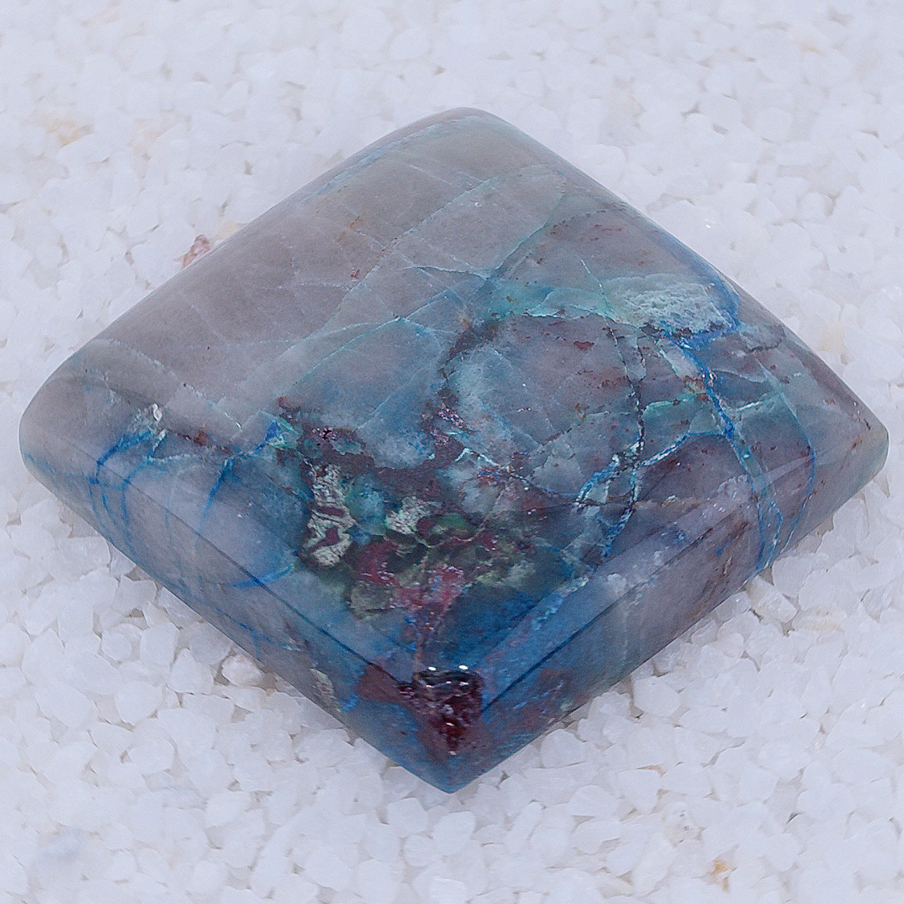 Rectangular Canyonite stone with blue and red patterns on a white textured background